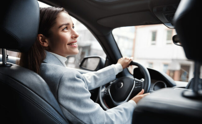 Happy elegant woman driver looking at person sitting in her car, pick up passenger. Businesswoman drop friend to meeting. Female executive talking to someone through car window