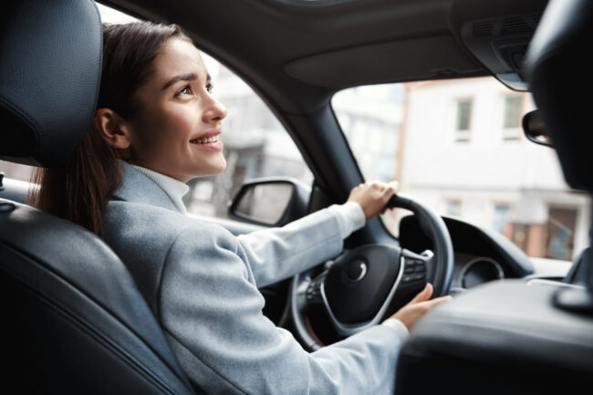 Happy elegant woman driver looking at person sitting in her car, pick up passenger. Businesswoman drop friend to meeting. Female executive talking to someone through car window